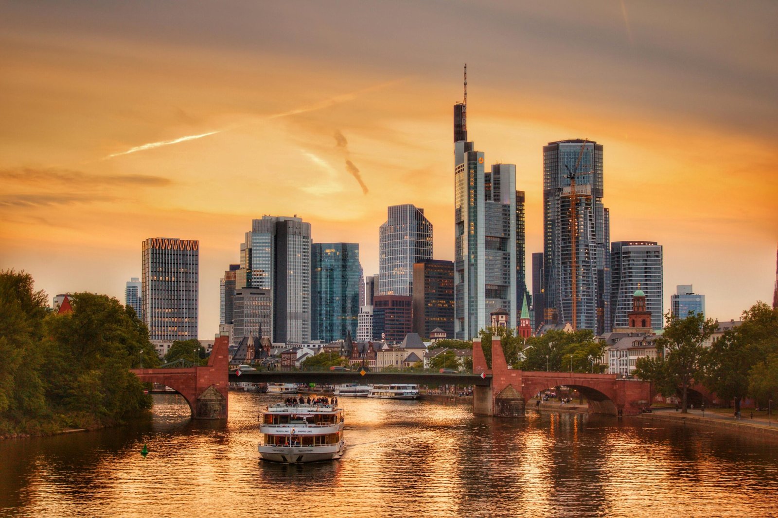 Stunning sunset over Frankfurt's skyline with a boat cruising on the Main River.